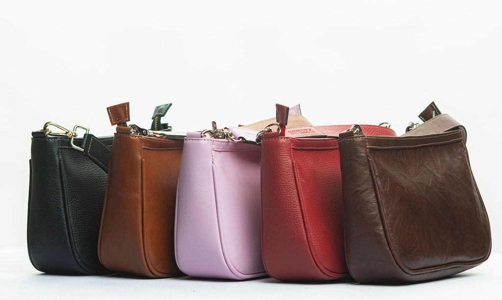 Bolsos de cuero Petros Leather en varios colores — negro, café, rosa, rojo y chocolate — alineados en fila, mostrando su diseño compacto y artesanal.